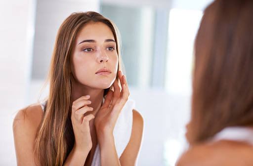 A woman looking in the mirror checking her cheek with her hand before going to Roane Family Dental in West Linn, OR.